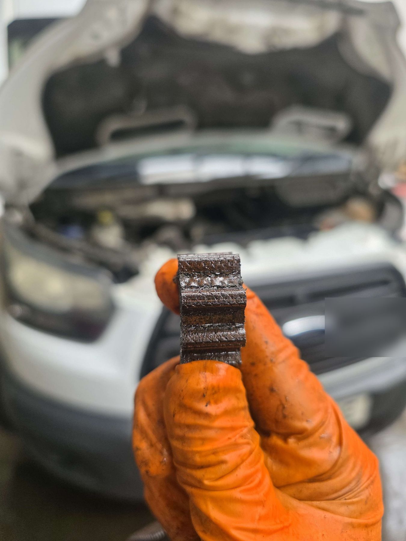 A worn Ford wet belt held up in front of a Transit being worked on
